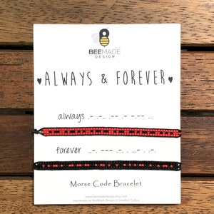 Pode incluir: Duas pulseiras de amizade com contas pretas e vermelhas que soletram "sempre" e "para sempre" em código Morse. As pulseiras são exibidas em um cartão branco com as palavras "Sempre & Para sempre" e "Pulseira de código Morse".