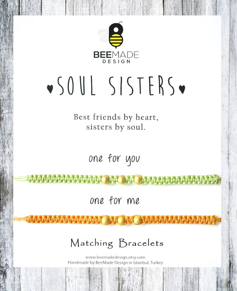 Pu&ograve; includere: Due braccialetti dell'amicizia con il testo "Soul Sisters" e "Best friends by heart, sisters by soul." I braccialetti sono verde e arancio con perline dorate. Il testo "one for you" e "one for me" &egrave; sopra i braccialetti.