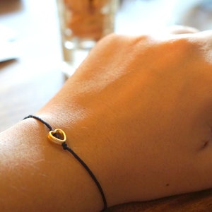May include: A simple black string bracelet with a gold heart charm.