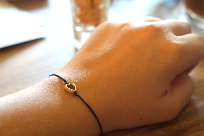 May include: A simple black string bracelet with a gold heart charm.