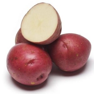 May include: A close-up of several red potatoes, one cut in half to reveal the pale yellow flesh. The potatoes have smooth, reddish-purple skin and are arranged on a white surface. The image highlights the fresh produce.