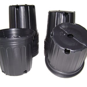May include: A collection of four black plastic plant pots. The pots are cylindrical with vertical ridges and drainage holes at the bottom. One pot is upright, while the others are tilted, showing their open tops and bottoms.