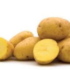 May include: A pile of fresh, unpeeled yellow potatoes against a white background. One potato is cut in half, revealing the yellow flesh. The potatoes vary in size and shape, with a few elongated and others more rounded.
