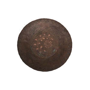 May include: A round copper plate with a decorative design of wheat stalks and a floral pattern. The plate has a dark brown patina and is slightly tarnished.