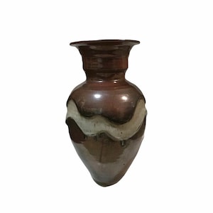 May include: A brown ceramic vase with a white glaze design. The vase has a rounded body and a flared opening.