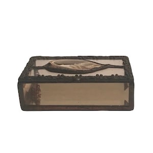 May include: A small, rectangular matchbox with a clear glass top and a black metal frame. The top of the box features a decorative design of a seashell.