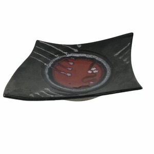 May include: A black ceramic serving dish with a red and white design. The dish has a slightly curved shape and a raised rim.