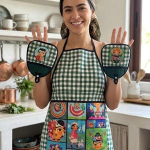 Puede incluir: Un delantal a cuadros verdes y blancos y manoplas a juego. El delantal presenta ilustraciones cuadradas coloridas de Frida Kahlo y otros diseños artísticos. Las manoplas tienen un retrato de Frida Kahlo sobre un fondo a cuadros verdes y blancos.