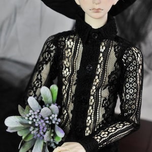 May include: A doll wearing a black lace shirt with a black hat and holding a bouquet of purple flowers. The doll has white hair and blue eyes. The doll is sitting on a wooden surface. The text "ROOM 18 R18M" is visible in the image.