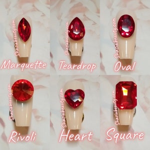 May include: Six different red nail art rhinestones in various shapes: marquette, teardrop, oval, rivoli, heart, and square.