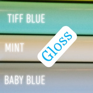 Op de afbeelding: Een verticale afbeelding met een selectie van kleurrijke materialen. De kleuren zijn geel, blauwgroen, mint, babyblauw en poederblauw. Het woord "Gloss" staat op een wit label. Het woord "SLIME" staat in witte letters boven het gele materiaal.