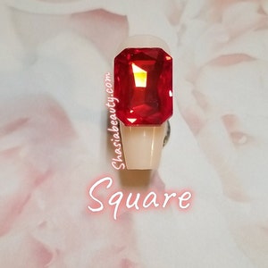 May include: A square-shaped, red, clear, faceted, gemstone on a white nail tip. The text "Square" is written below the nail tip.