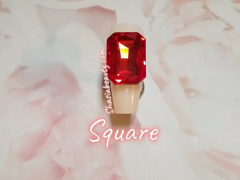 May include: A square-shaped, red, clear, faceted, gemstone on a white nail tip. The text "Square" is written below the nail tip.