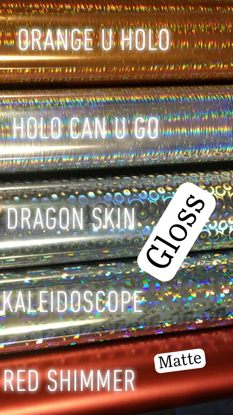 Op de afbeelding: Close-up van verschillende rollen decoratief vinyl met diverse afwerkingen. De rollen bevatten "Orange U Holo", "Holo Can U Go", "Dragon Skin", "Kaleidoscope" en "Red Shimmer". De afbeelding bevat ook de woorden "Gloss" en "Matte".