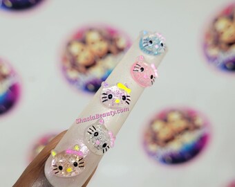 May include: Close-up of a long, white, artificial fingernail with a pink, blue, and grey Hello Kitty character design. The nail is decorated with glitter and rhinestones.