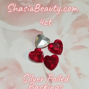 May include: Four red heart-shaped rhinestones with silver foiled backings. The rhinestones are on a white background with the text "ShasiaBeauty.com 4ct Silver Foiled Backings".