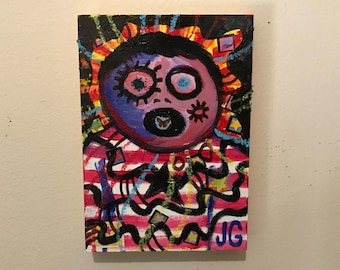 May include: A colorful abstract painting on canvas with a pink face with black eyes and a black mouth. The face is surrounded by a red, yellow, and blue background with black lines and shapes. The painting is signed "JG" in the bottom right corner.
