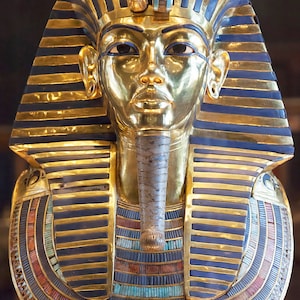 May include: A gold mask of an Egyptian pharaoh with a blue and gold headdress, a blue and gold collar, and a blue and gold beard. The mask is decorated with turquoise and red stones.