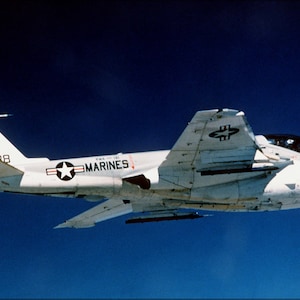 May include: A white and gray Grumman A-6 Intruder aircraft with the words "US Marines" on the side. The aircraft has a black knight's head and the letters "VK 88" on the tail.