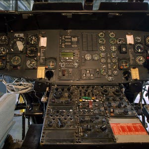 May include: A close-up view of a helicopter cockpit with a variety of gauges and controls. The cockpit is dark grey and the gauges are black with white numbers and markings.