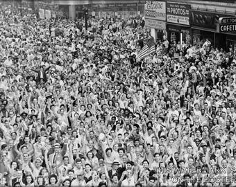May include: A black and white photo of a large crowd of people gathered in a city street. The people are all looking up at something, and many of them are waving their hands in the air. There are buildings in the background, and some signs are visible.