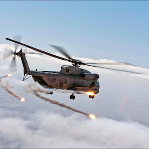 May include: A grey military helicopter flying through the clouds, with smoke trails coming from the back of the helicopter.