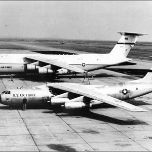 May include: Two large, white military cargo planes, a C-5 Galaxy and a C-141 Starlifter, are parked on a tarmac. Both planes have the words "U.S. AIR FORCE" printed on the side.