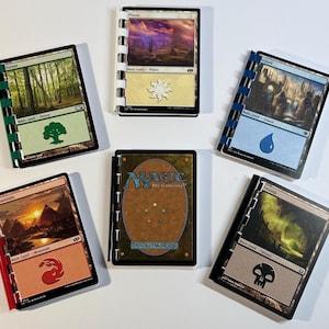 May include: A collection of Magic: The Gathering trading cards, each bound with a colored spine. The cards feature various landscape illustrations and symbols, including a forest, mountain, and swamp. The central card displays the Magic logo.