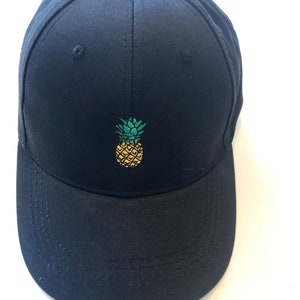 May include: A black baseball cap with a yellow and green embroidered pineapple on the front.