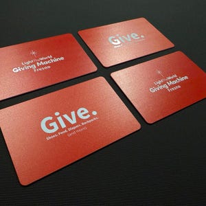 May include: Four rectangular red cards with rounded corners. Two cards feature the white text LightTheWorld Giving Machine Fresno with a star icon. Two cards feature the white text Give. followed by Shoes. Food. Diapers. Backpacks. (and more).