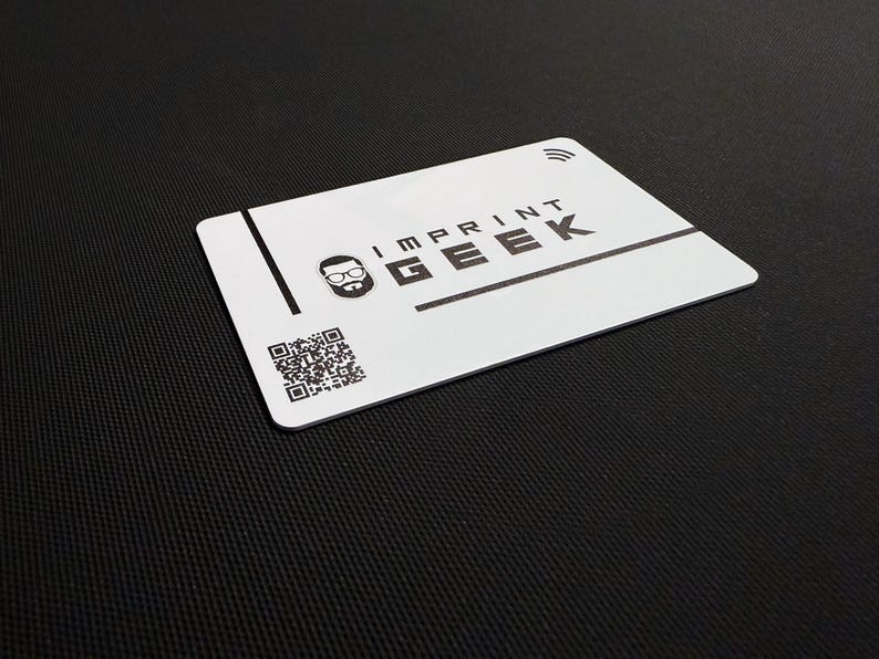 May include: A white card with the text "IMPRINT GEEK" in black, a logo of a bespectacled face, and a QR code. It also has a contactless payment symbol. The card is on a black textured background.