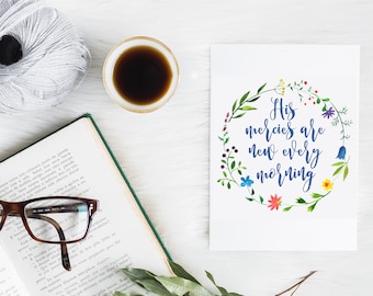 May include: A white card with a watercolour floral wreath and the text "His mercies are new every morning". The card is on a white surface with a book, glasses, a cup of coffee, and a ball of yarn.