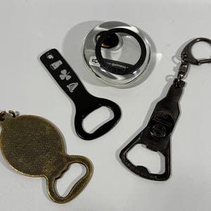 May include: An assortment of bottle openers in various designs. Includes a black bottle opener with a shamrock design, a bronze-colored bottle opener, a bottle opener shaped like a beer bottle, and a silver-colored bottle opener.