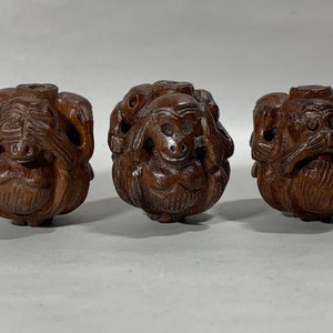 May include: Three wooden carvings of monkeys, each with a different gesture: one covering its eyes, one covering its ears, and one covering its mouth. The monkeys are carved in a traditional style and have a dark brown color.