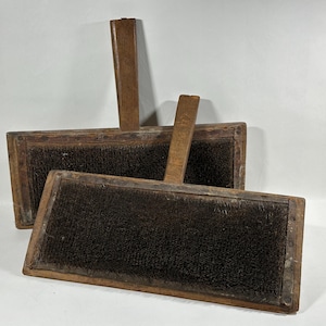 May include: Two wooden wool carding tools with a brown wooden handle and a dark brown bristled surface.