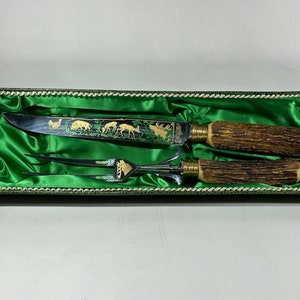 May include: A set of two kitchen utensils with stag horn handles in a green velvet lined box. The knife and fork have gold and green etched designs of animals.