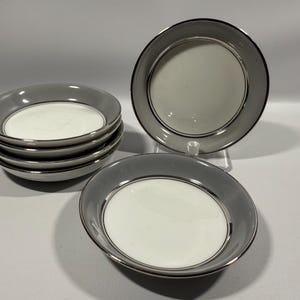 May include: Set of four gray and white ceramic bowls with silver trim. The bowls are stacked on top of each other.