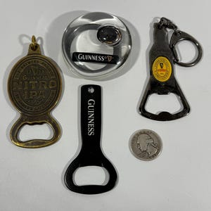 May include: A collection of Guinness-branded bar accessories, including a bottle opener keychain, a round bottle opener, and a black bottle opener. Also includes a brass Nitro IPA bottle opener and a quarter.