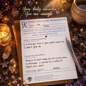 May include: A white paper sheet titled Daily Self-Care Prescription with blue text and lines. It includes fields for name and date, plus sections for daily reminders and self-affirmations. A silver pen with a crystal-filled barrel rests on the paper.