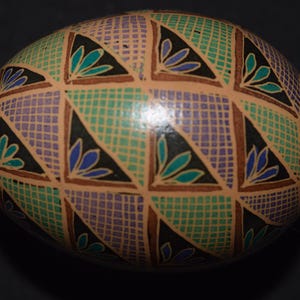 May include: A hand-painted Easter egg with a geometric pattern of green, purple, and brown triangles. The egg is decorated with black and blue floral designs.