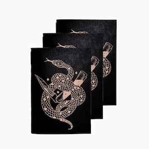 May include: Three black art prints featuring a beige illustration of a snake coiled around a dagger. The snake's body is detailed with scales and stars. The prints are stacked slightly, revealing the design on each.
