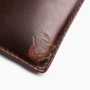 Peut inclure: Gros plan sur un portefeuille en cuir marron avec un bord cousu et un motif de serpent en relief.