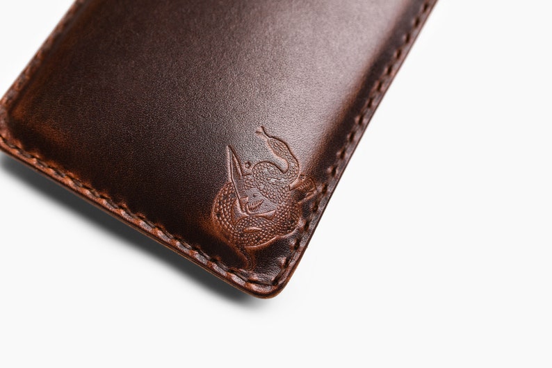 Peut inclure: Gros plan sur un portefeuille en cuir marron avec un bord cousu et un motif de serpent en relief.