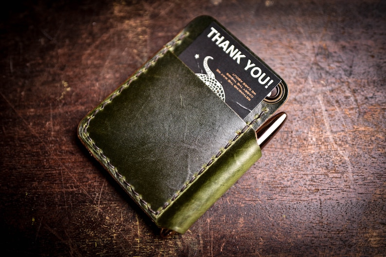 May include: A green leather wallet with a stitched edge and a card slot. The wallet has a pen holder and a card inside with the text "Thank You!" printed on it.