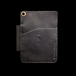 Peut inclure: Portefeuille en cuir noir avec une seule poche et un rabat cousu. Le portefeuille a un anneau en laiton et le texte "HITCH & TIMBER" en relief sur le c&ocirc;t&eacute;.