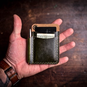 May include: A green leather wallet with a brown leather flap and a pen holder. The wallet has a card slot and a money pocket. The text "HIGH & TIBER" is embossed on the front of the wallet.