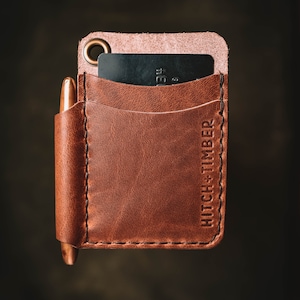 May include: A brown leather wallet with a pen holder and a card slot. The wallet has the text "HITCH + TIMBER" embossed on the side.