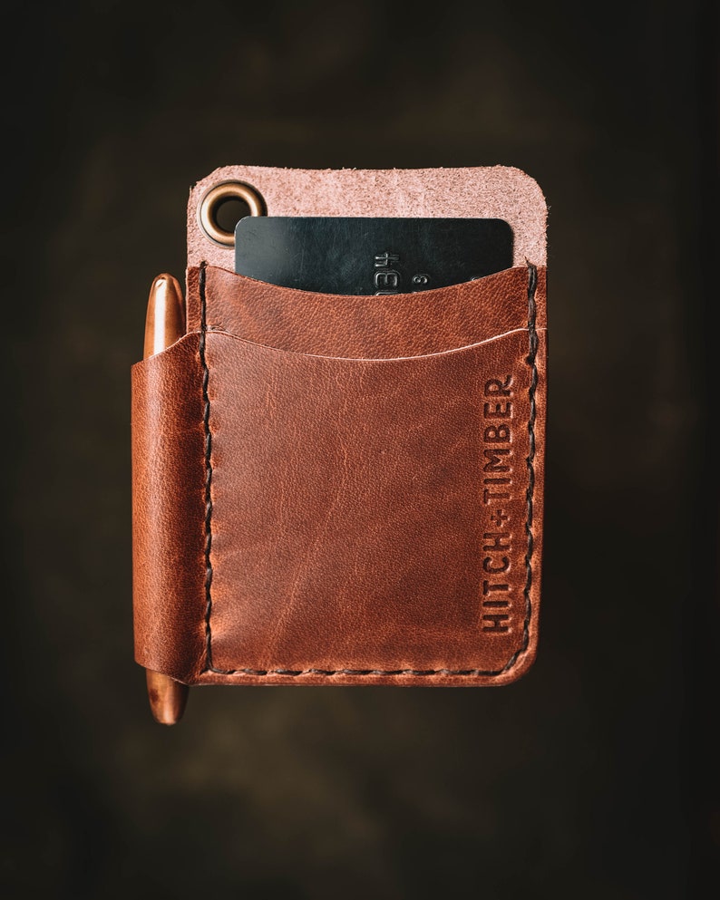 May include: A brown leather wallet with a pen holder and a card slot. The wallet has the text "HITCH + TIMBER" embossed on the side.