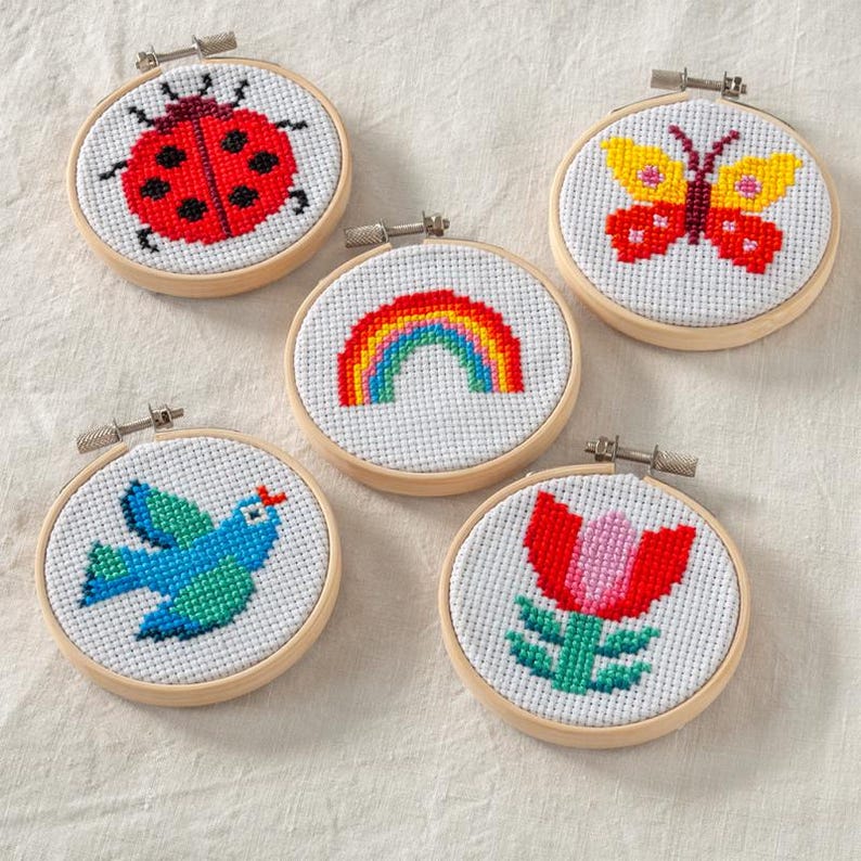 five completed cross stitch kits with bluebird, flower, butterfly, ladybird and rainbow designs