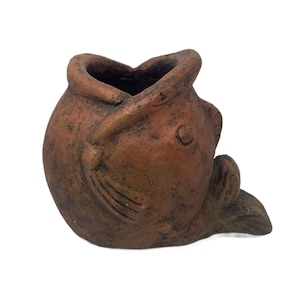 May include: A terracotta-colored fish-shaped planter with a wide opening. The planter has a textured surface and a small fin detail. The fish's mouth is open, and it has a small eye detail. The planter is designed to sit on a flat surface.